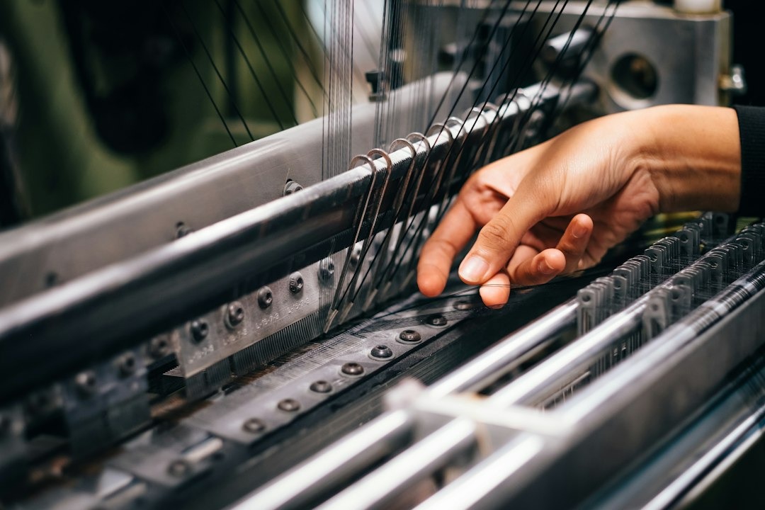 Hand guides black threads through an industrial textile machine.